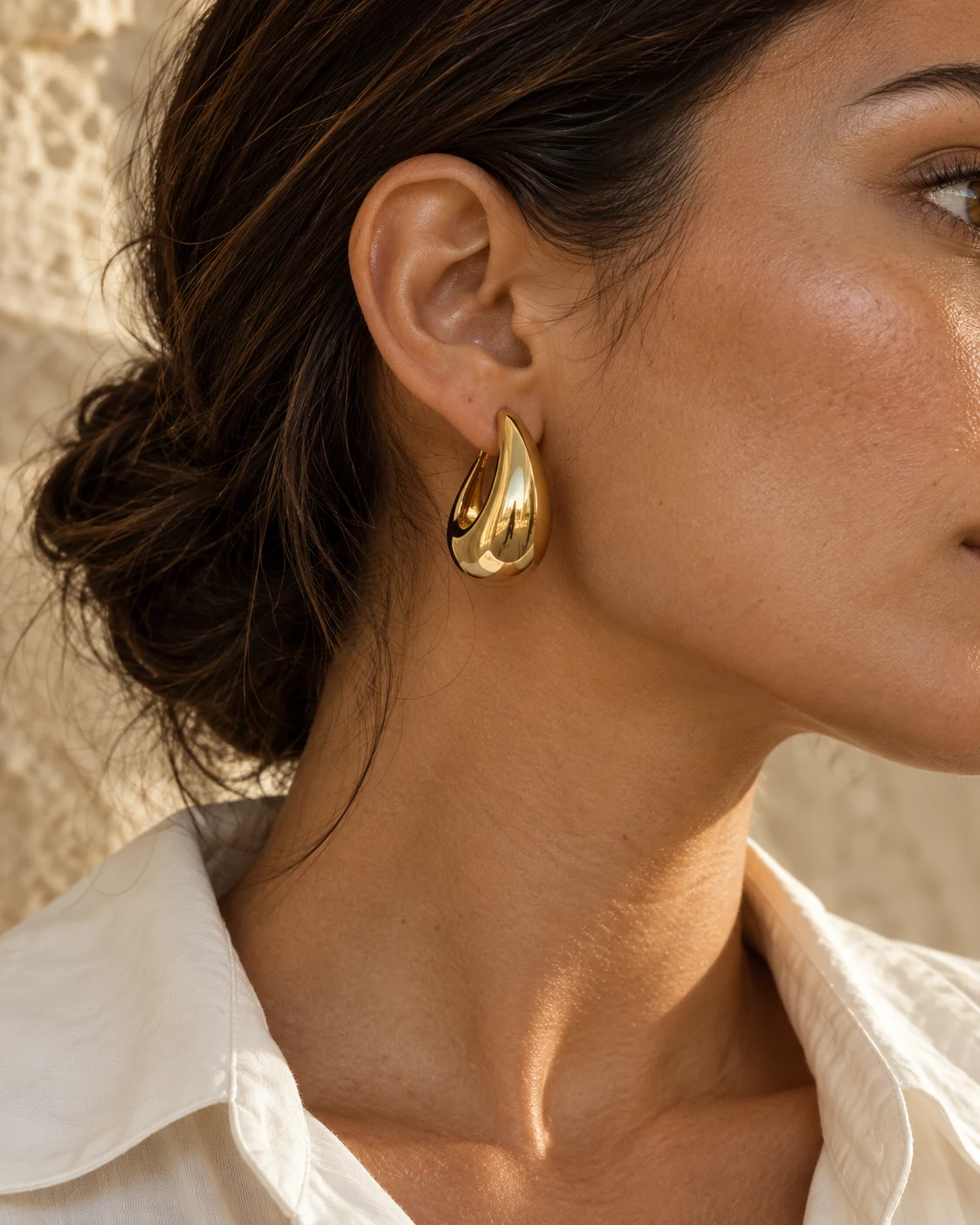 Close-up of a sculptural gold hoop earring worn with hair tucked behind the ear